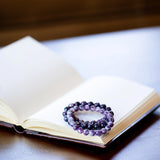 The Evoline Lepidolite Serenity & Emotional Balance Bracelets stacked on a mediation book.