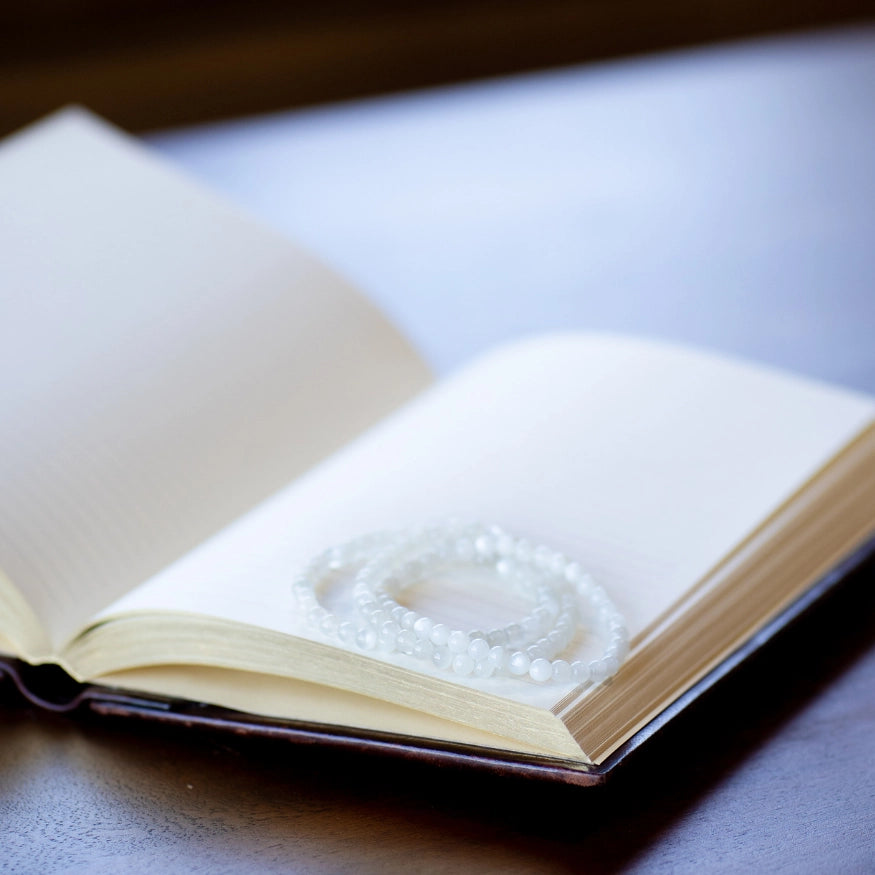 The Evoline Moonstone Bracelets stacked on a mediation book.