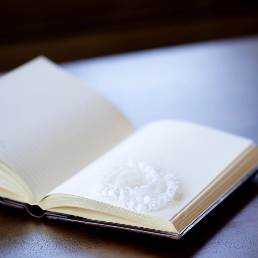 The Evoline Selenite Cleansing & Higher Light Connection Bracelets stacked on mediation book.