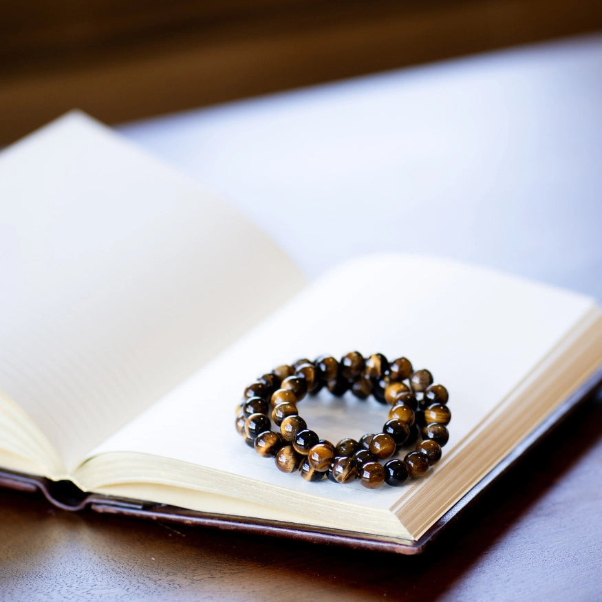 The Evoline Tigers Eye Courage and Clarity Bracelets stacked on a meditation book.