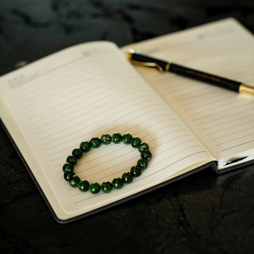 Diopside Green beaded bracelet on an open notebook with a pen